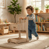 Toddler playing with wooden Montessori toy walker in sunny, organized playroom with bookshelves.