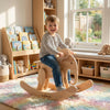 Smiling child on handcrafted wooden elephant rocker in Montessori-inspired playroom with books and toys.