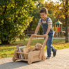 Smiling boy pushes handcrafted Montessori wooden cart with books and teddy bear outdoors