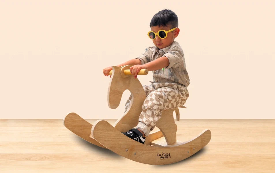 Smiling child on handcrafted wooden elephant rocker in Montessori-inspired playroom with books and toys.