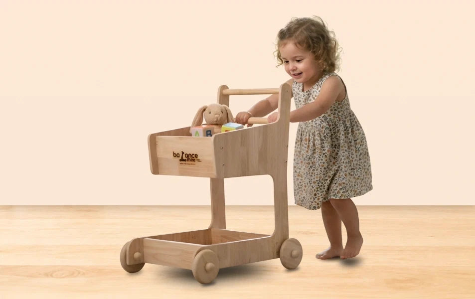 Toddler playing with wooden Montessori toy walker in sunny, organized playroom with bookshelves.