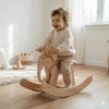 Smiling toddler on handcrafted wooden rocking elephant in Montessori-inspired playroom