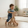 Smiling toddler rides handcrafted wooden Montessori balance bike indoors
