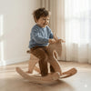 Smiling child riding a handcrafted Montessori wooden rocking horse in a sunlit room